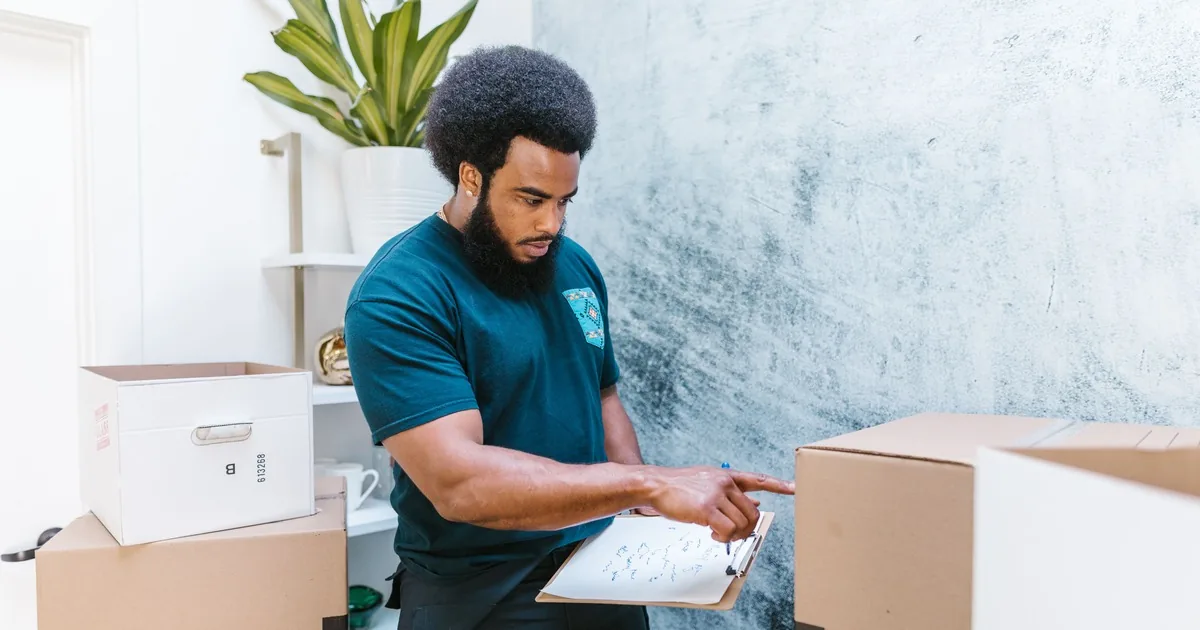Mover reviewing an inventory sheet beside packed boxes inside a residence