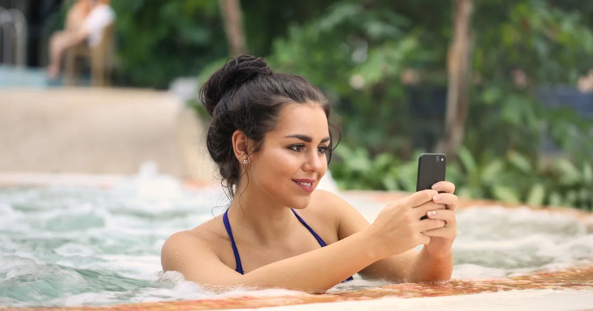 Woman using a smartphone while sitting beside an outdoor spa