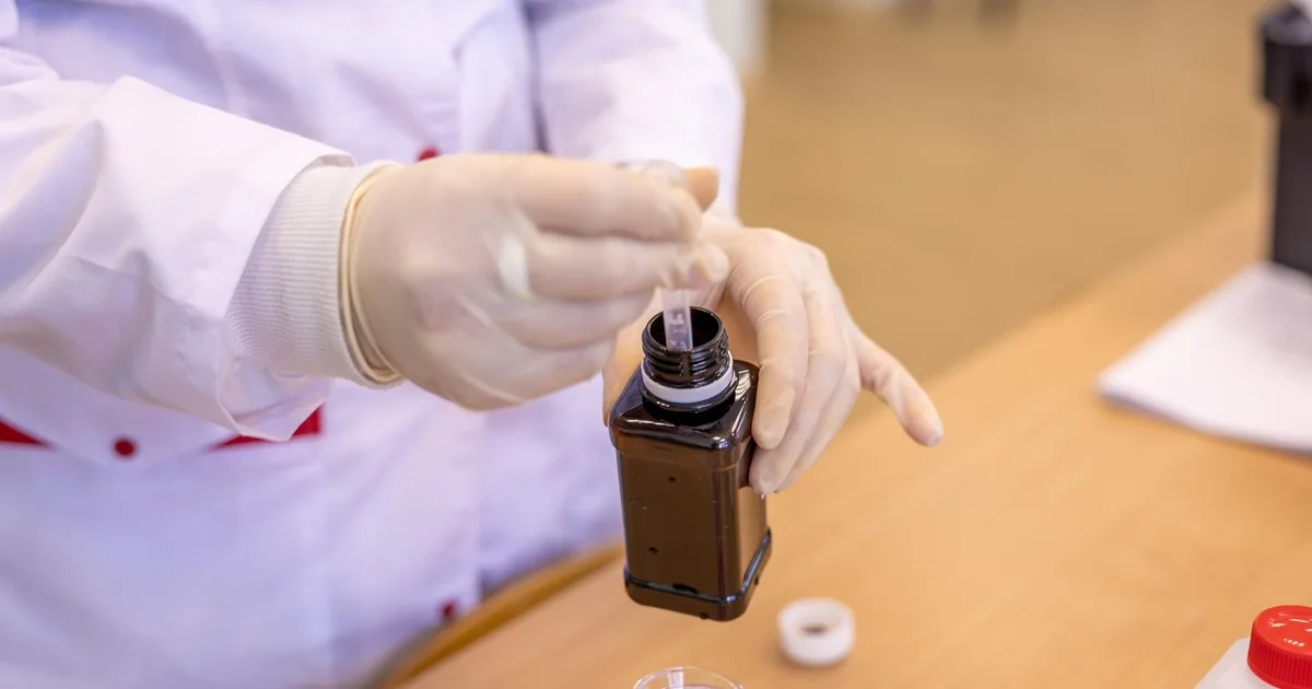 Laboratory professional extracting a clear liquid sample from a bottle